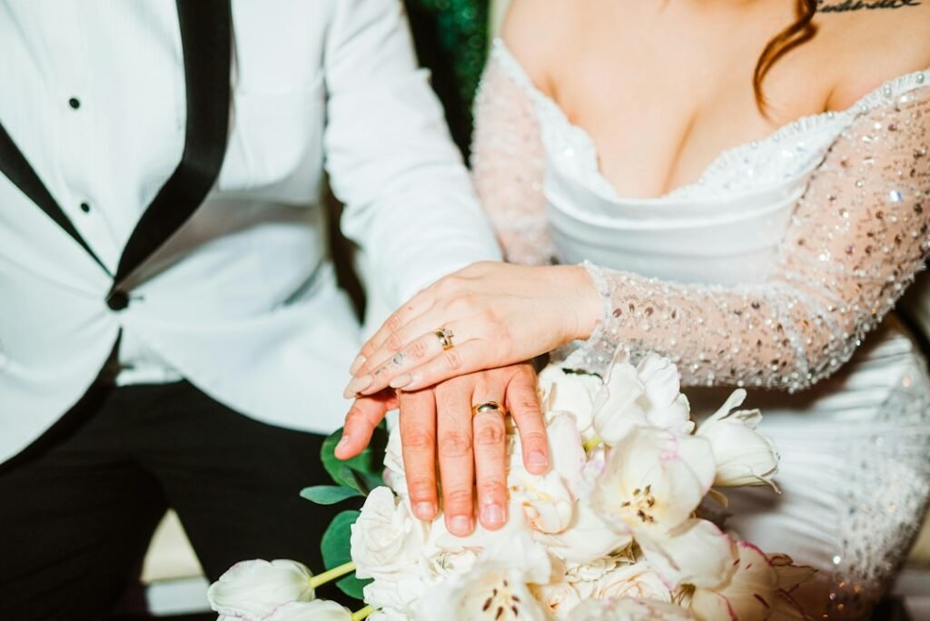 Newly married couple holding hands with wedding rings and bouquet