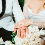 Newly married couple holding hands with wedding rings and bouquet